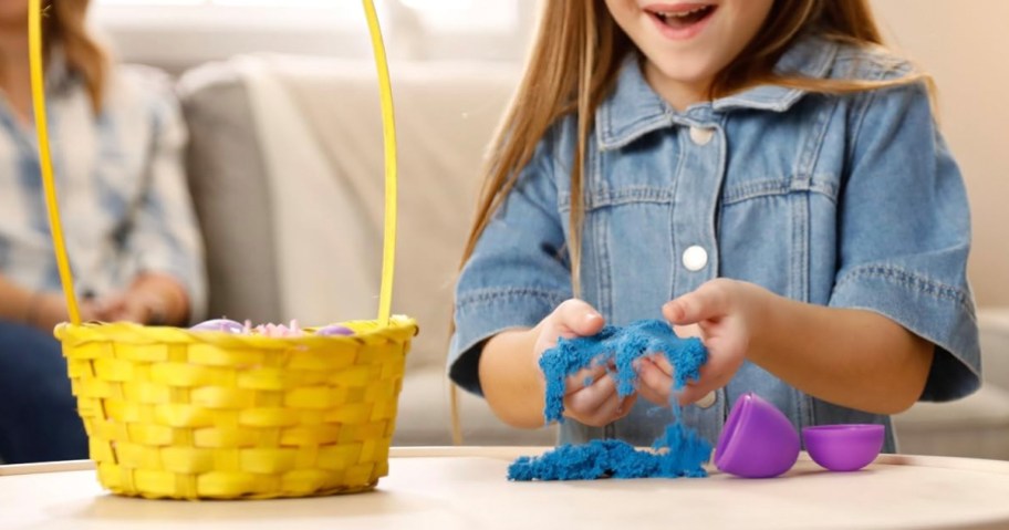 girl opening easter egg with kintic sand inside next to yellow easter basket