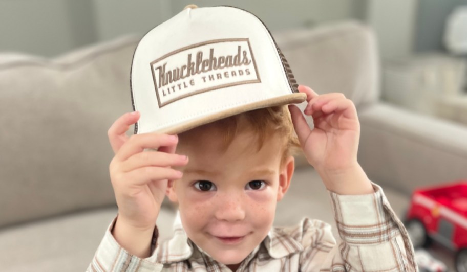 little boy lifting trucker hat off head