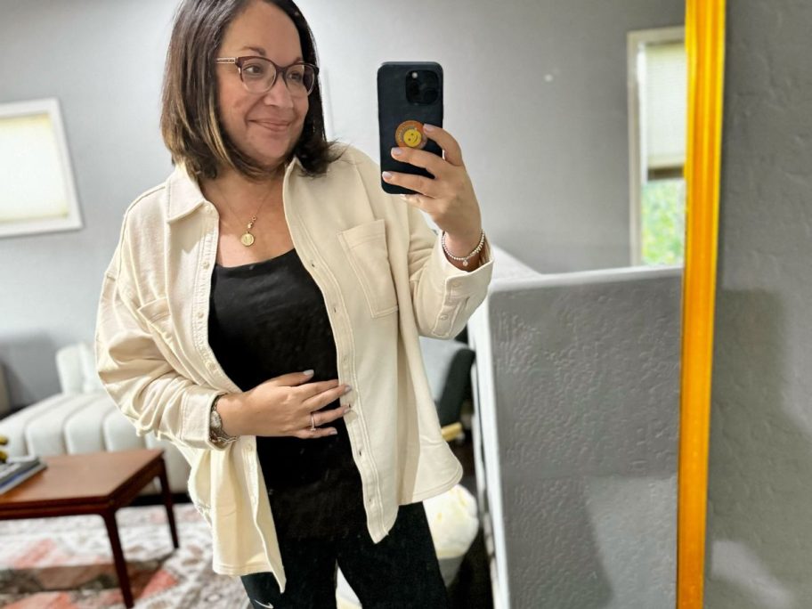woman taking selfie in mirror with beige shacket and black top
