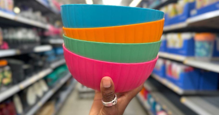 a womans hand holding a stack of 4 cereal bowls in blue orange green and fuchsia