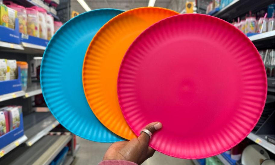 a womans hand holding fanned out blue, orange and fuchsia plastic plates 