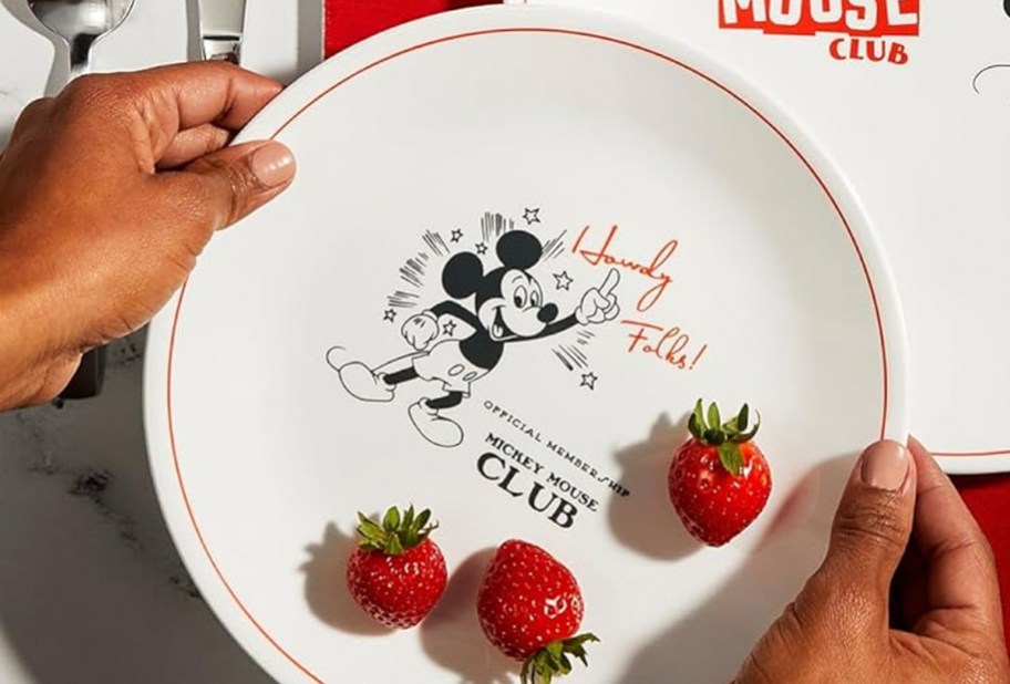 hands holding disney corelle mickeymouse plate with strawberries on top