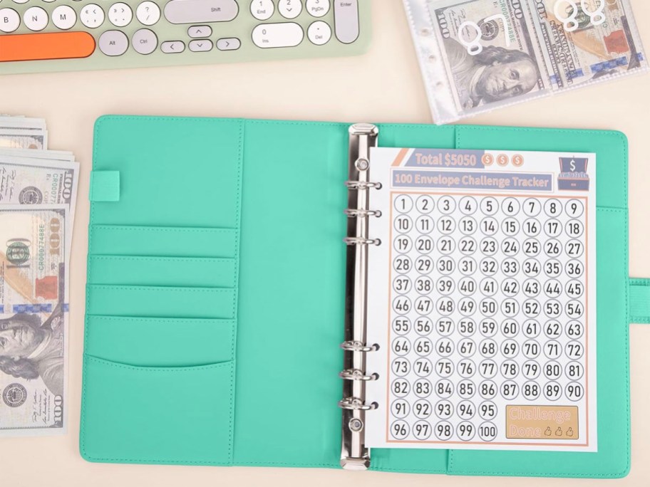 teal money saving binder open with tracker with money laying next to it