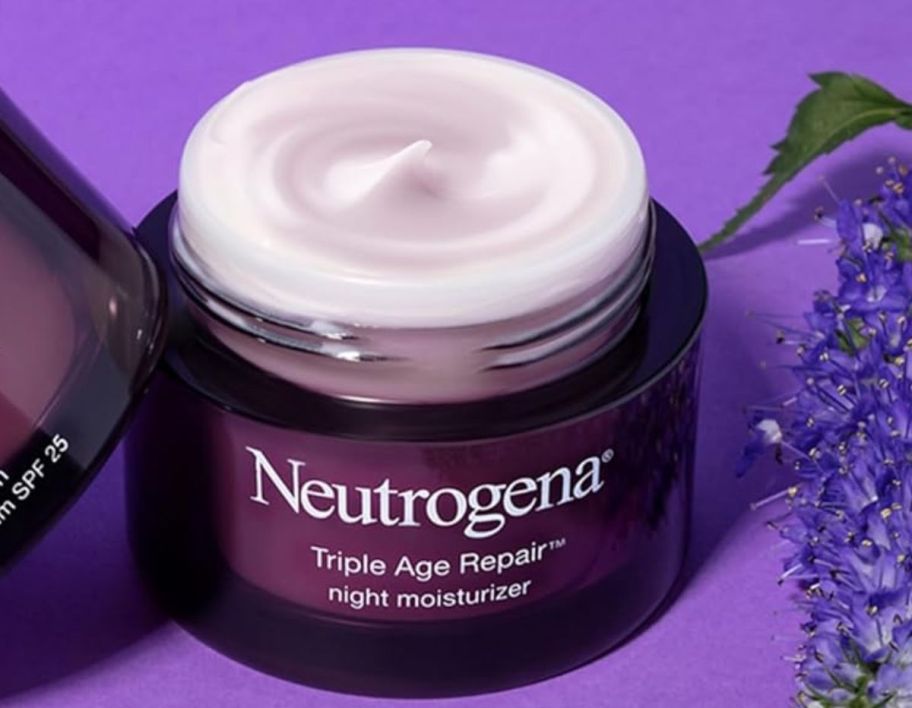 a jar of neutrogena triple repair night cream on a purple background next to a srpig of lavender