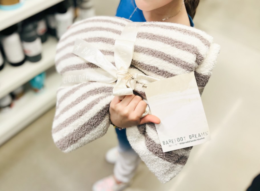 young girl standing in a nordstrom rack store aisle, holding a barefoot dreams blanket