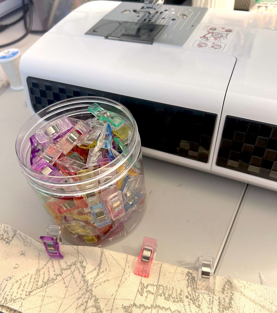 clear jar of plastic clips in front of sewing machine and on edge of map fabric