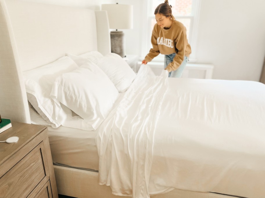 woman making bed with white sheets