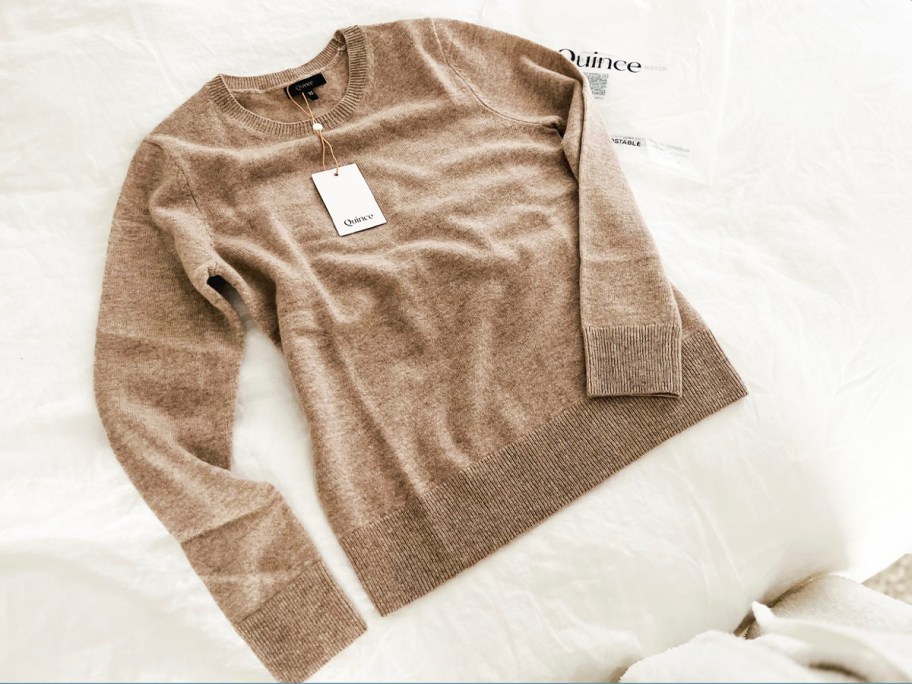 tan cashmere sweater laying on bed with quince bag