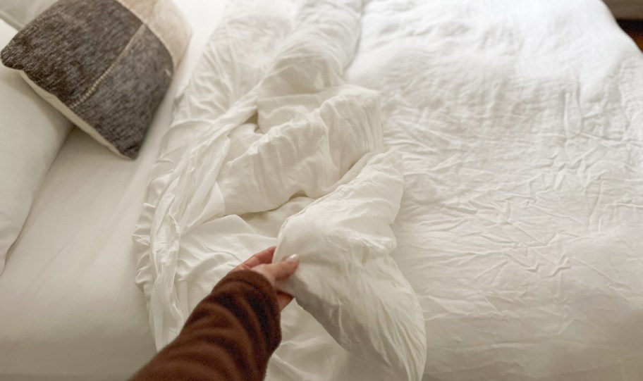 hand holding corner of white duvet on bed