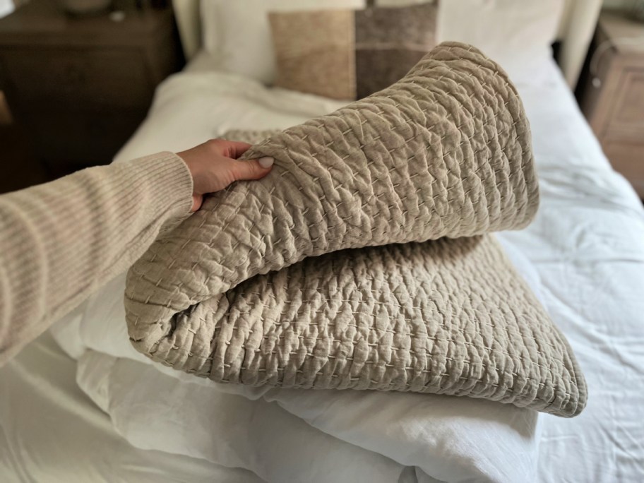 hand touching a quince linen quilt that's folded on a bed