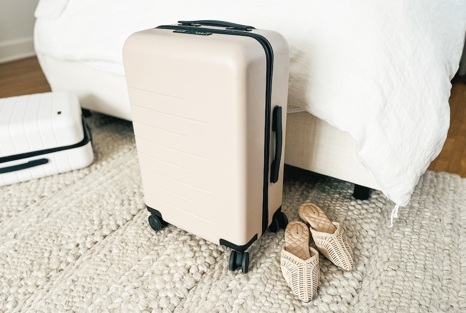 tan luggage suitcase on rug next to sandals