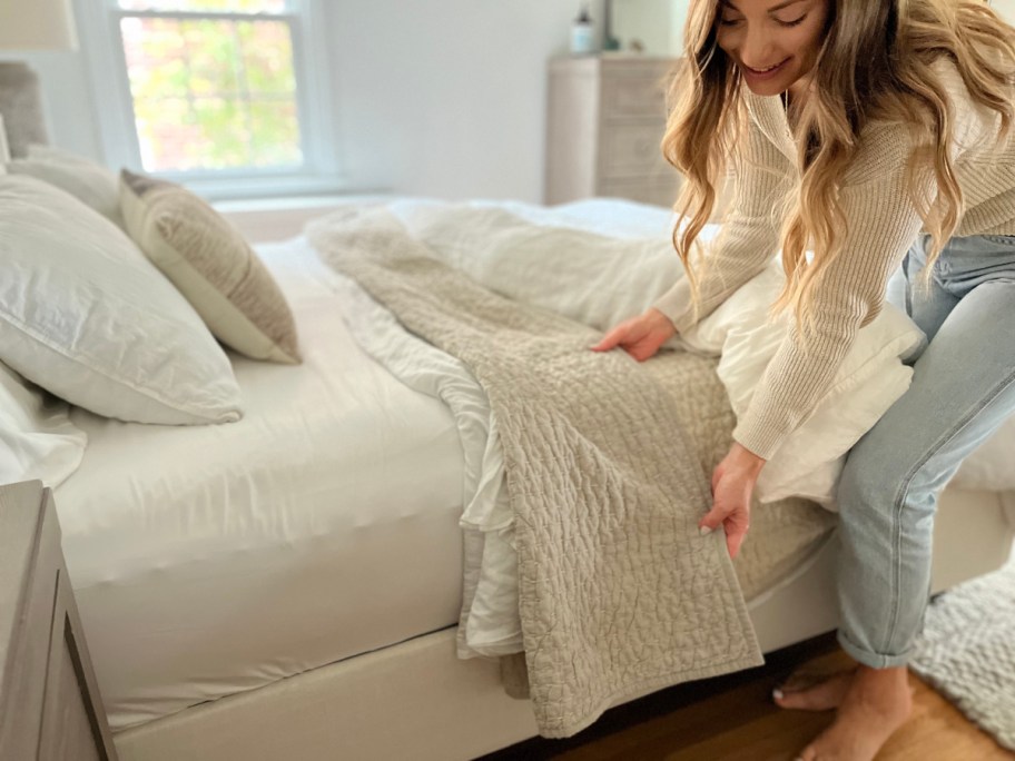 smiling woman adjusting quince bedding in a sunny bedroom