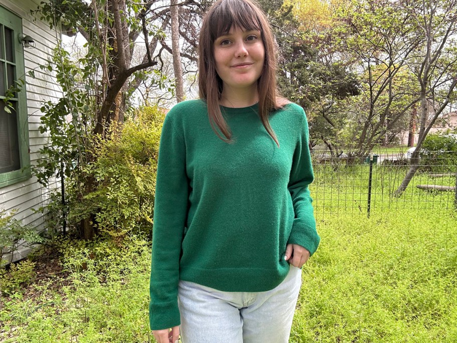woman wearing green cashmere sweater with trees and grass behind her
