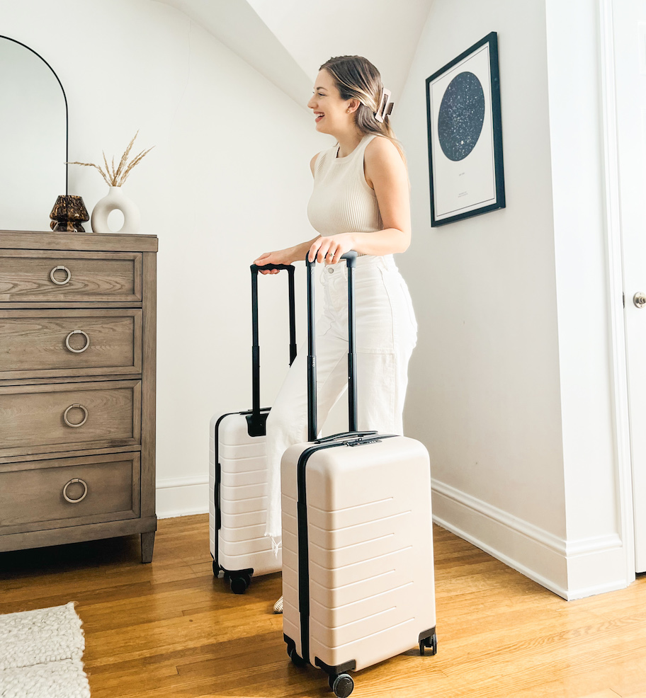 woman smiling holding handles of white and beige carry on sized luggage