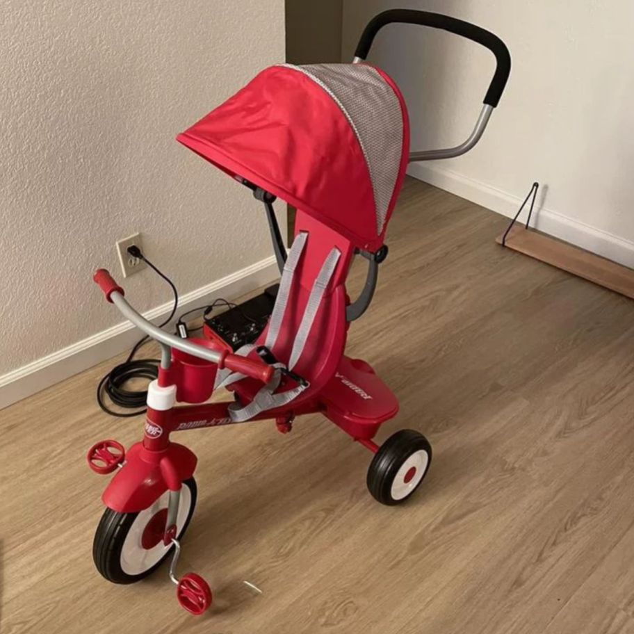 a red radio flyer stroll and trike in a room with a hardwood floor