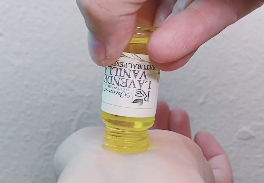 Hands tipping perfume oil bottle on wrist