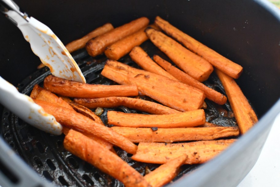 roasted carrots in an air fryer with tongs after cooking