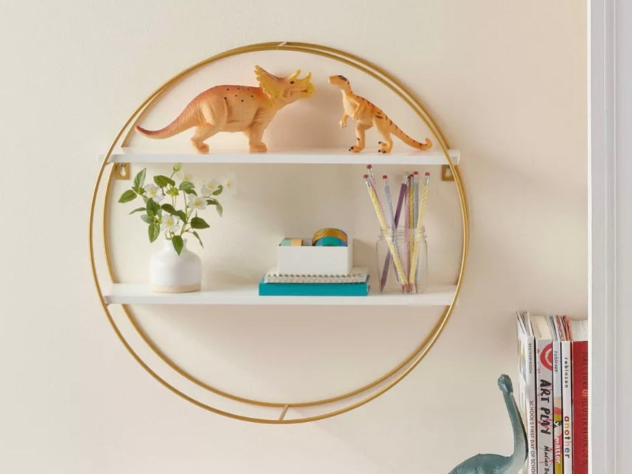 gold round shelf hanging on wall with dinorsaur toys and plant sitting on it