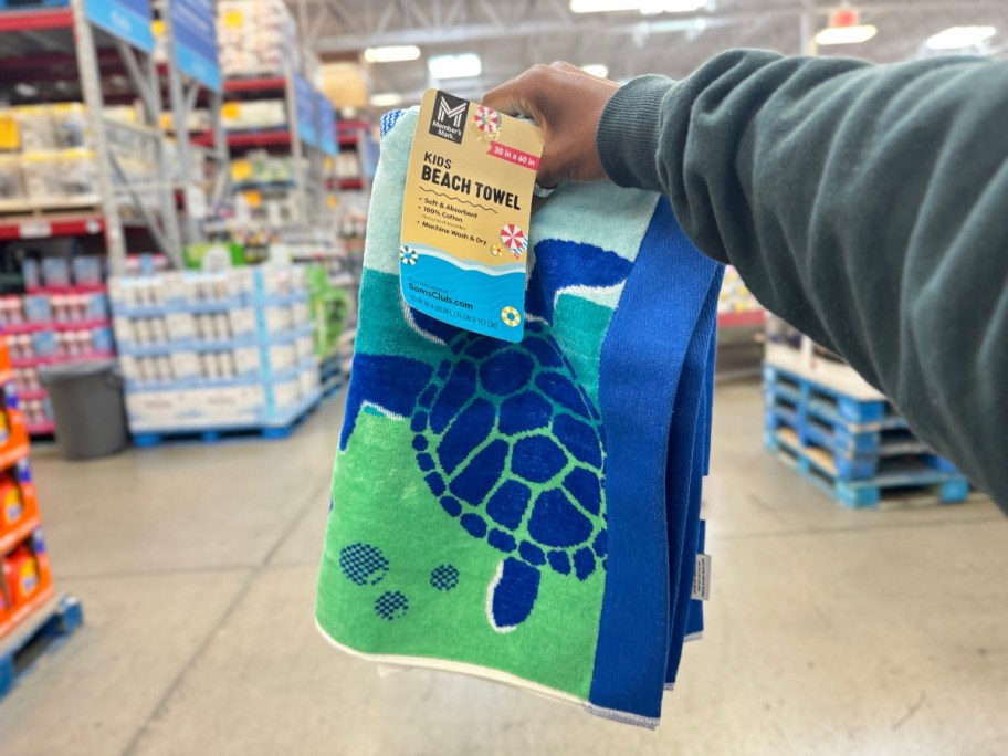 hand holding a kid's beach towel with blues, greens and turtles on it