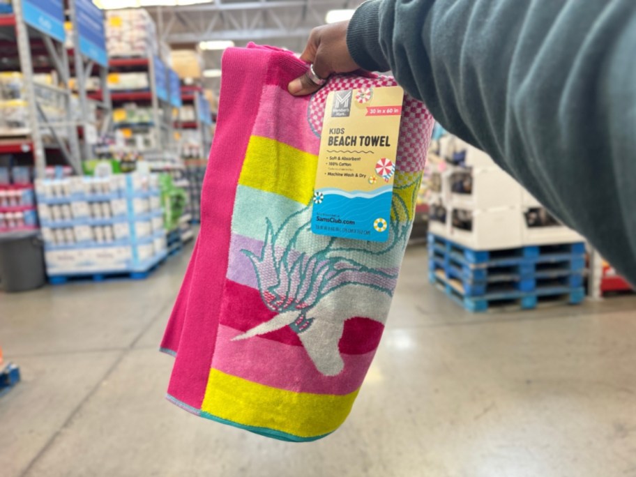 hand holding a kid's beach towel with pink, purple, green, white stripes and a unicorn on it