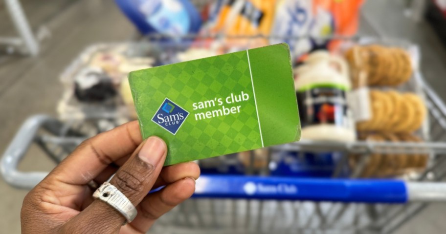 hand holding a sams club membership in front of a store cart