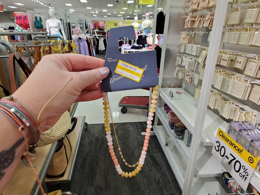 hand holding up a beaded necklace with a clearance sticker in store