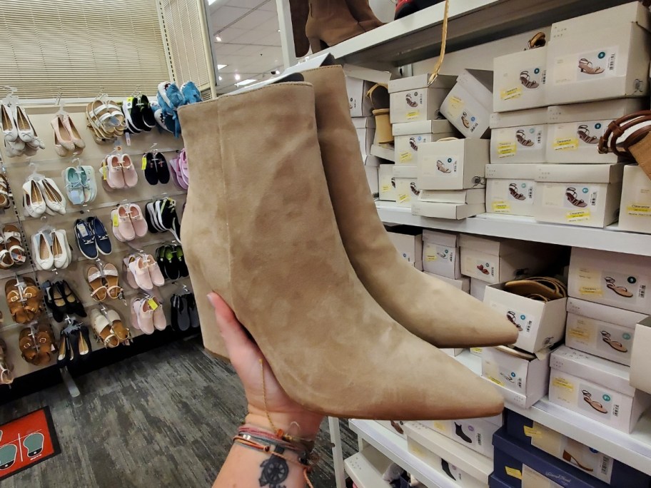 woman's hand holding a tan pair of women's pointed toe boots in store