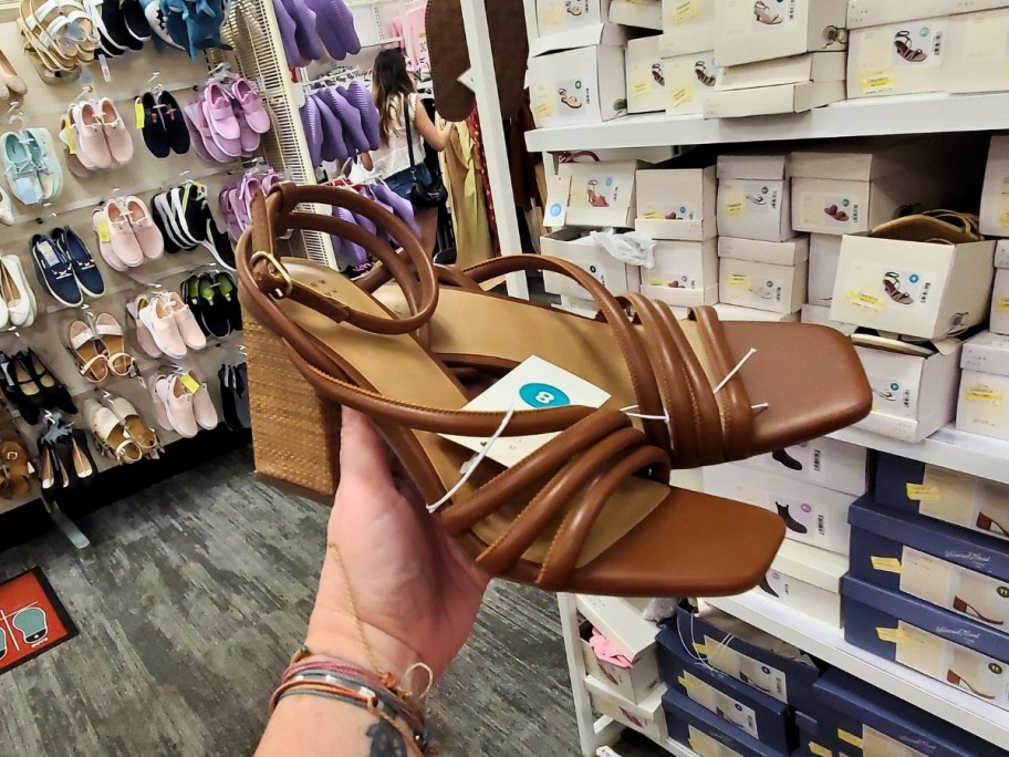 hand holding a pair of brown strappy heel women's shoes in a store