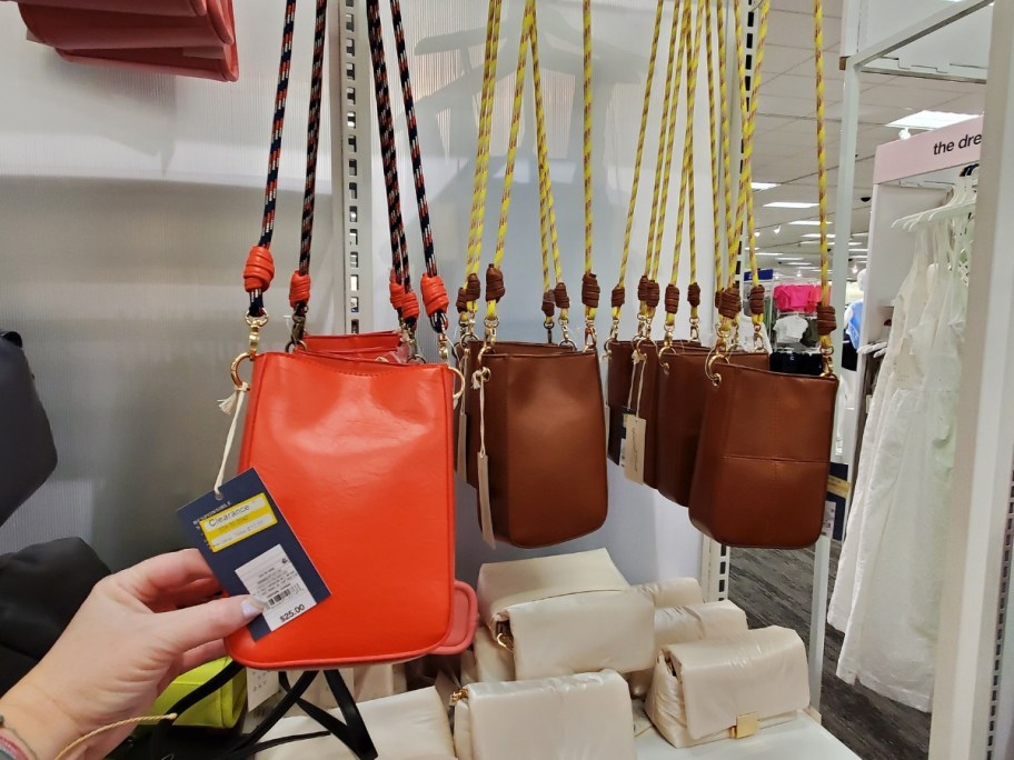 hand reaching for an orange crossbody bag on display in store