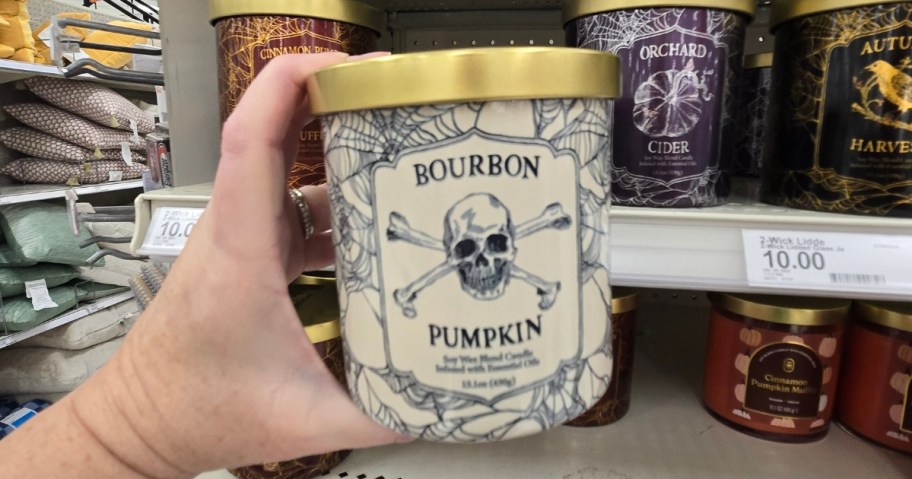 hand holding a jar candle with a gold lid and a white and blue label with a skull on it, more Halloween candles in the background