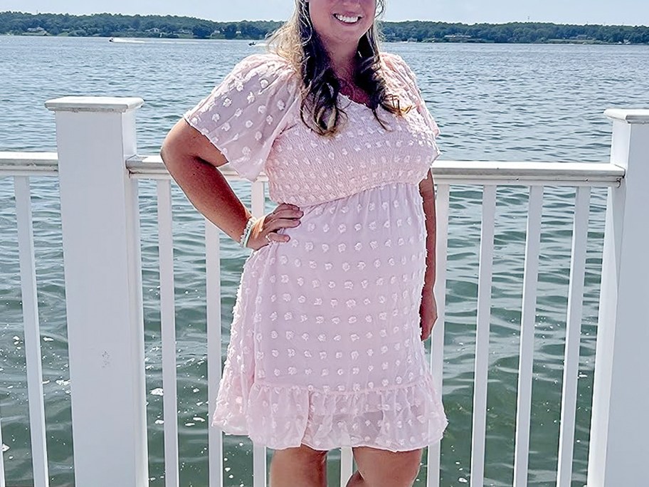 woman wearing light pink dress near water and white fence