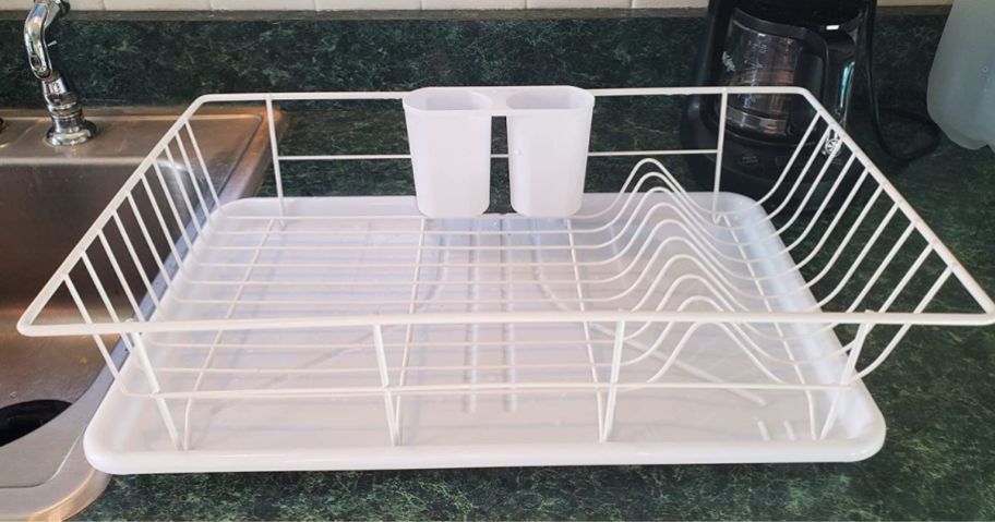 a white dish draining rack on a green counter top next to a stainless steel sink