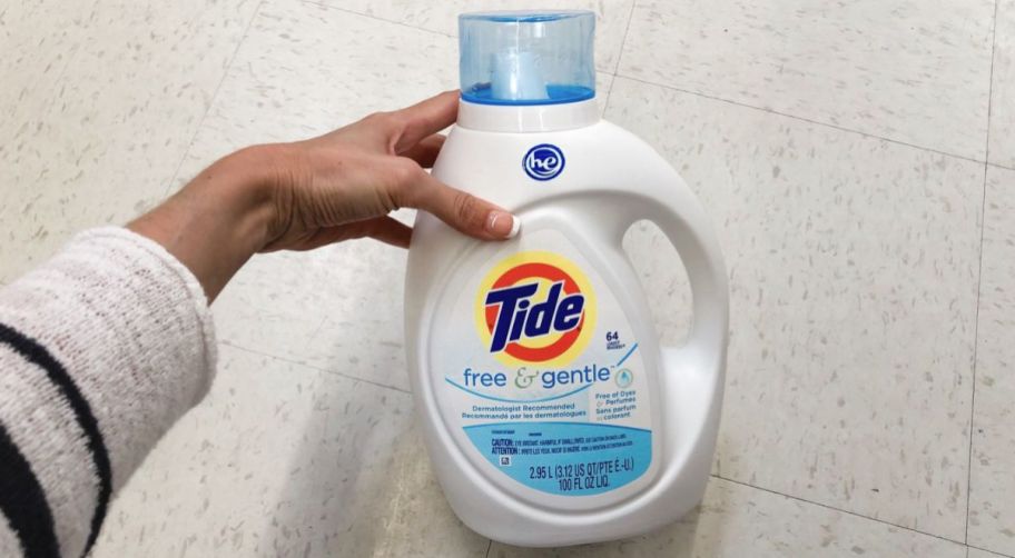 a womans hand holding a jug of tide free and clear laundry detergent