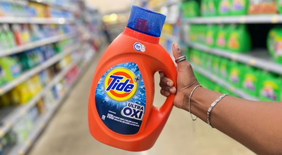a womans hand holding a jug of tide ultra oxi liquid laundry detergent