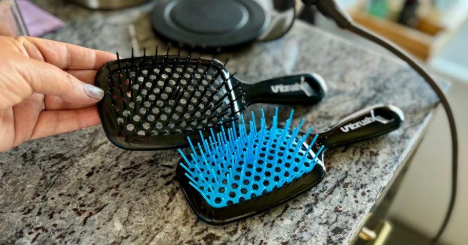 a black and a blue & black UNbrush hairbrushes on a counter with person's hand reaching for it
