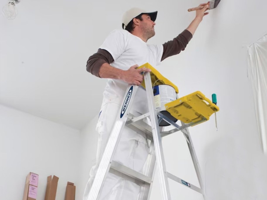 man standing and painting on yellow and aluminum ladder