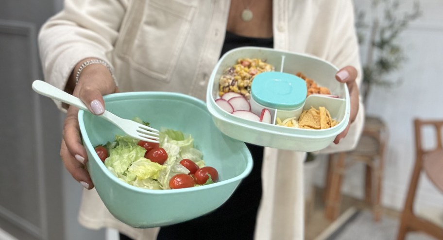 woman holding two salad containers with food inside of it