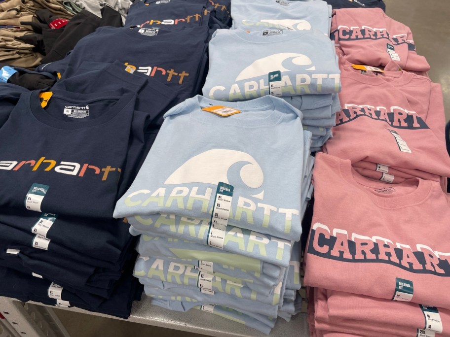 various colors and styles of Men's Carhartt Tees on a display table at Sam's Club