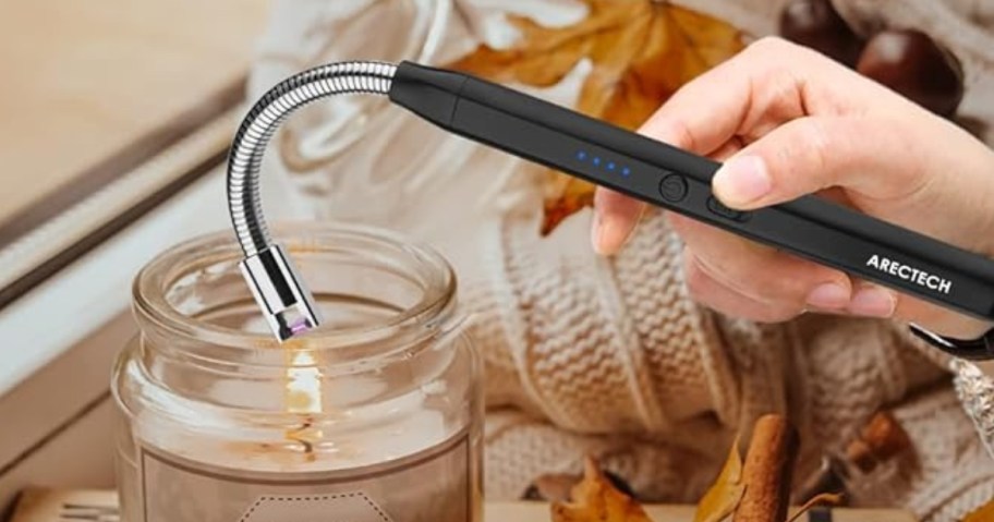 person lighting a candle with a black and silver electric candle lighter