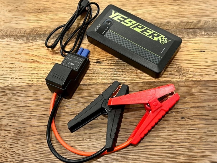 Yesper Battery Jumpstarter pack with cables and usb cable laying on wood table