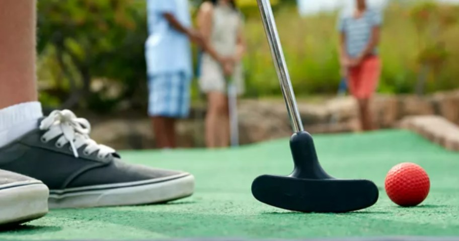 kids feet, golf putter and ball on a mini golf course