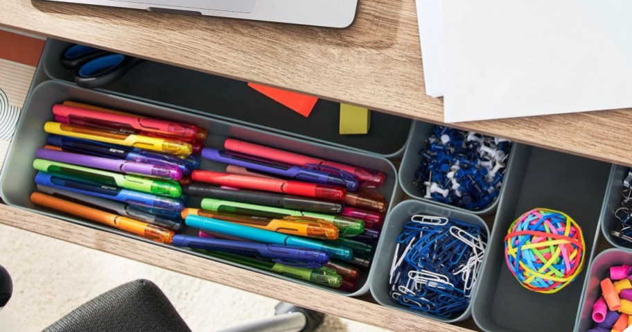 open desk drawer with grey organizers filled with office supplies