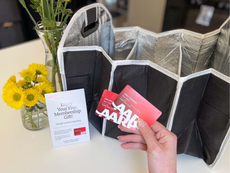 person holding AARP cards with trunk organizer and membership pamphlet and sunflowers in vase on counter