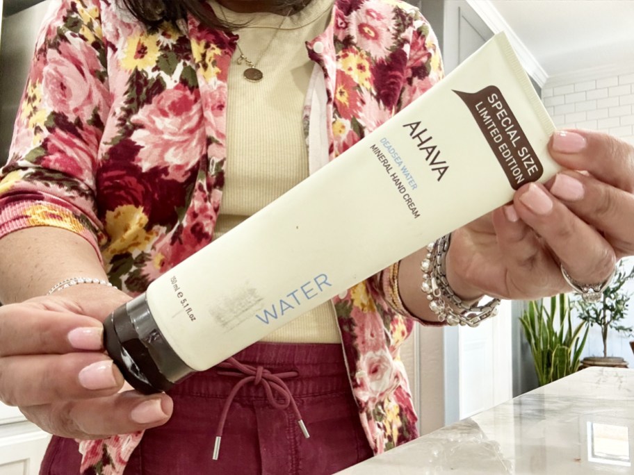 woman holding up a large white bottle of ahava hand cream