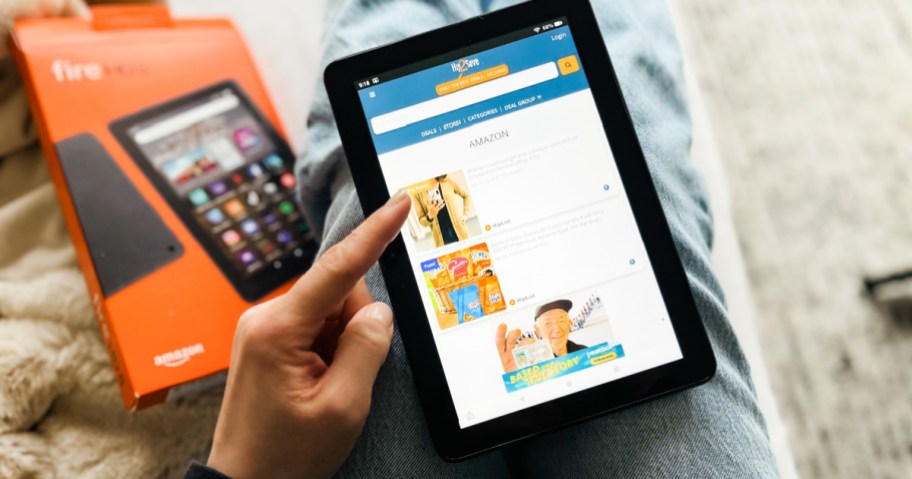 Person scrolling Hip2save on Amazon tablet near packaging
