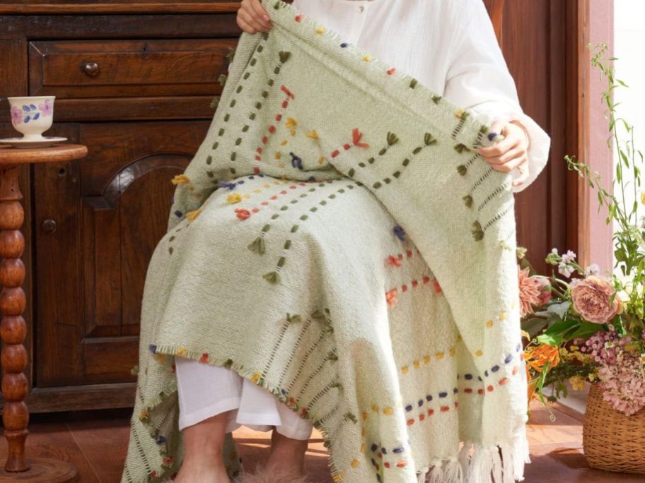 A woman sitting in a chair with an Amélie Home Boho Throw Blanket 