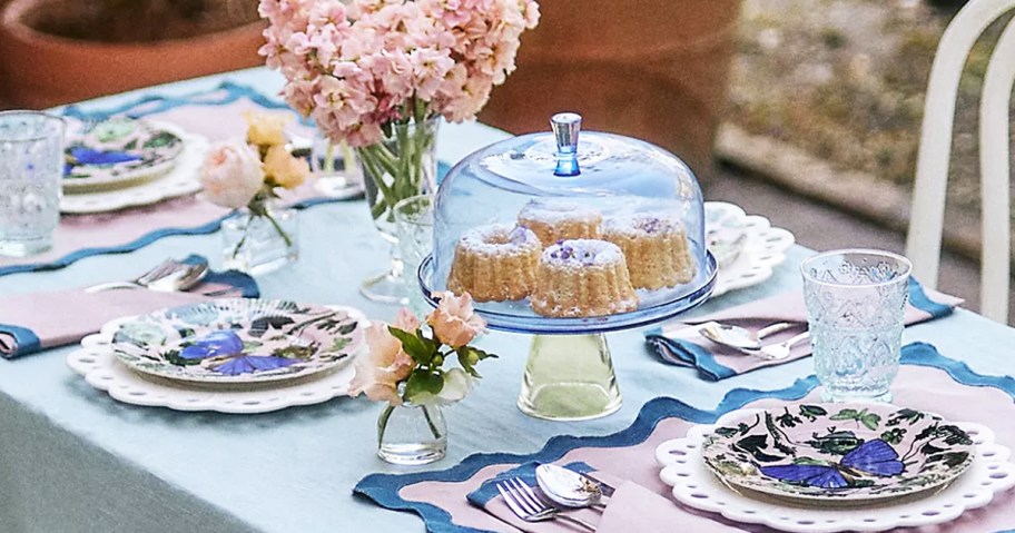 table set with plates, silverware, cake stand, and vase of flowers