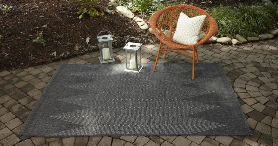 A gray rug outside with patio furniture on it. 