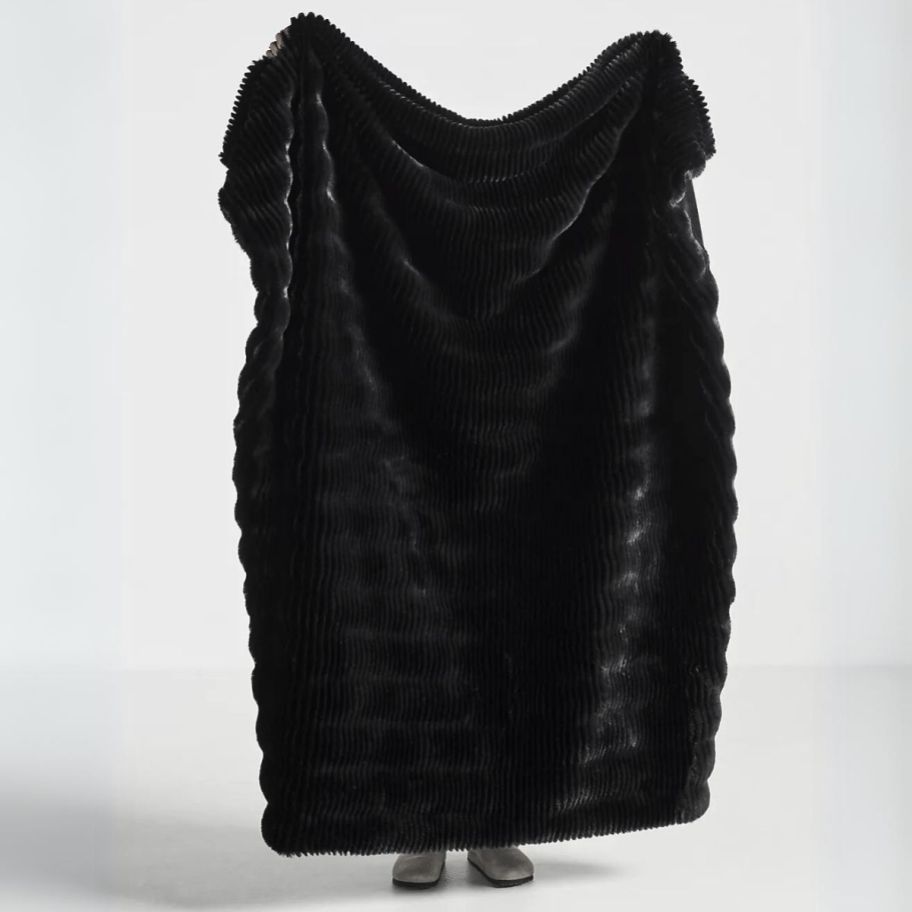 a person standing behind and holding up a large black faux fur throw blanket