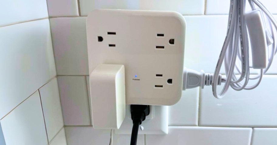 outlet extender with multiple outlets with various electronics plugged into it on a white subway tile wall